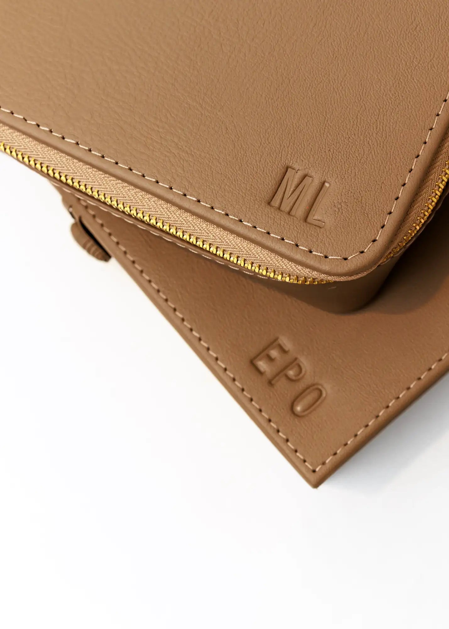 Bolsa de cuero marrón con cremallera de tono dorado y bordes cosidos, con iniciales ’ml’ grabadas en relieve en la pieza superior.