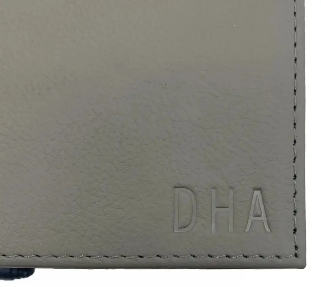 Cartera de cuero gris con logo 'dha' en relieve y costuras visibles a lo largo del borde.