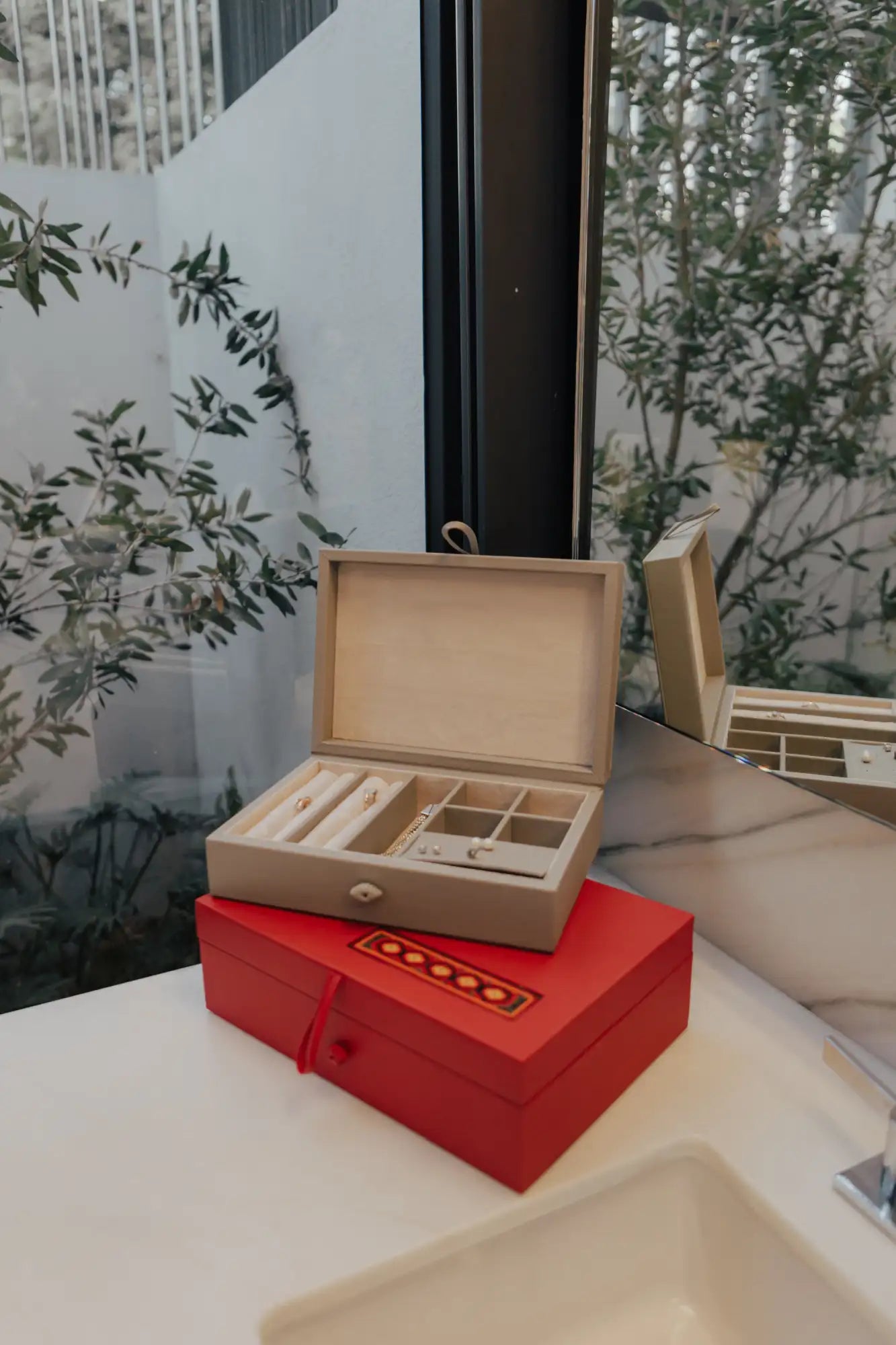 Caja de joyas de cuero beige con compartimentos interiores y una pequeña perilla en la parte delantera.