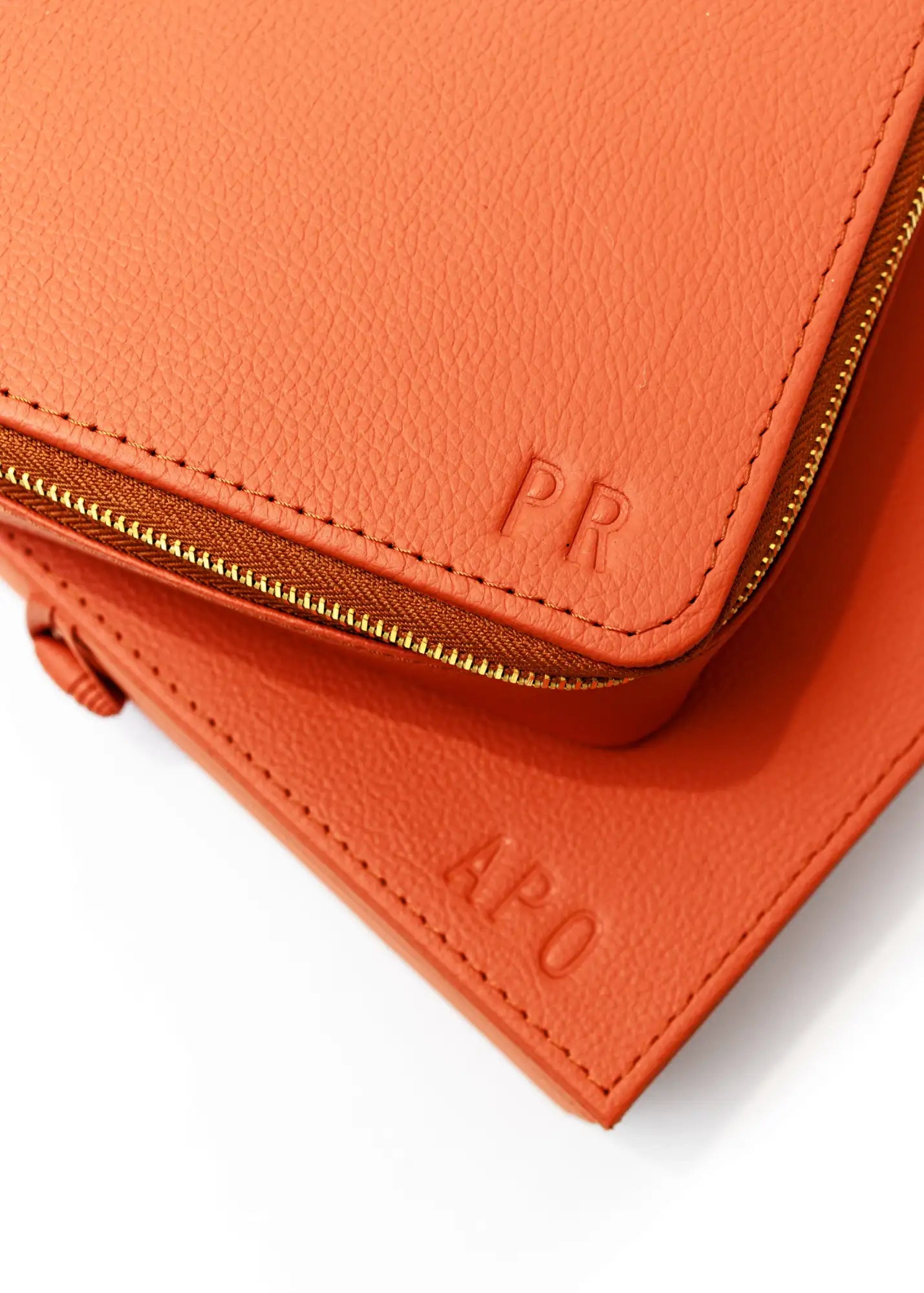 Cartera de cuero naranja con cremallera, iniciales en relieve y cremallera en tono dorado.