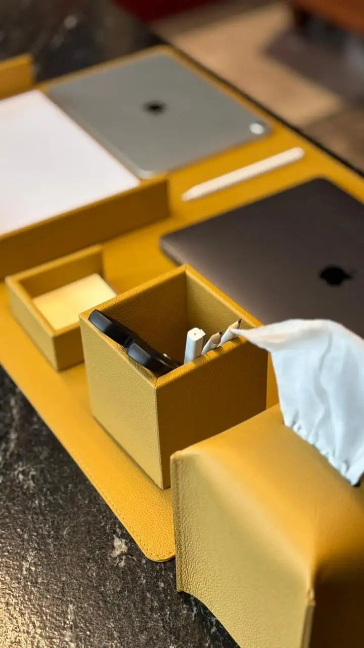 Organizador de escritorio de cuero amarillo con múltiples compartimentos que contienen bolígrafos, una caja de pañuelos y papelería.